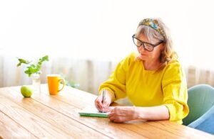 Older woman writing notes at a kitchen table in natural light